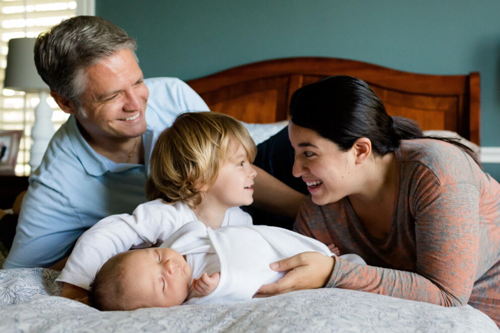 Eine Familie, die gemeinsam auf einem Bett liegt und miteinander lacht.